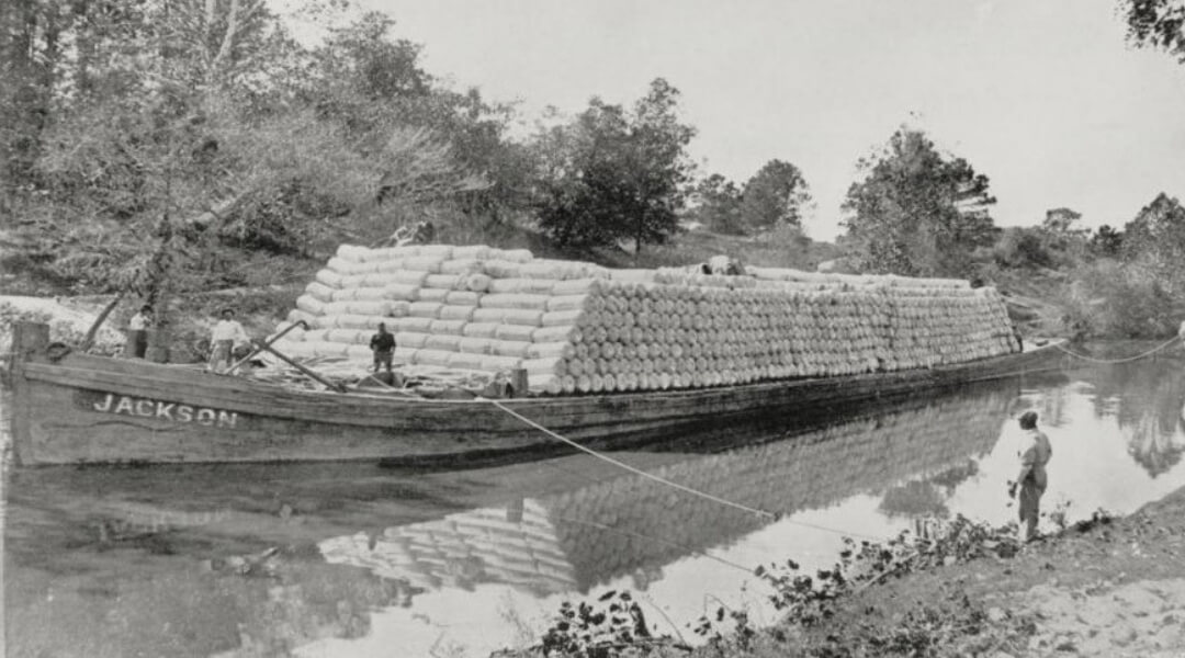 Old photo of ship carrying load passing through channel.