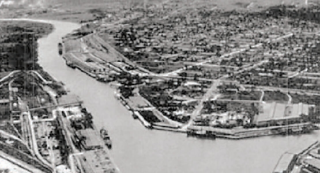 Aerial photo of ship channel and growing city around it in black and white.